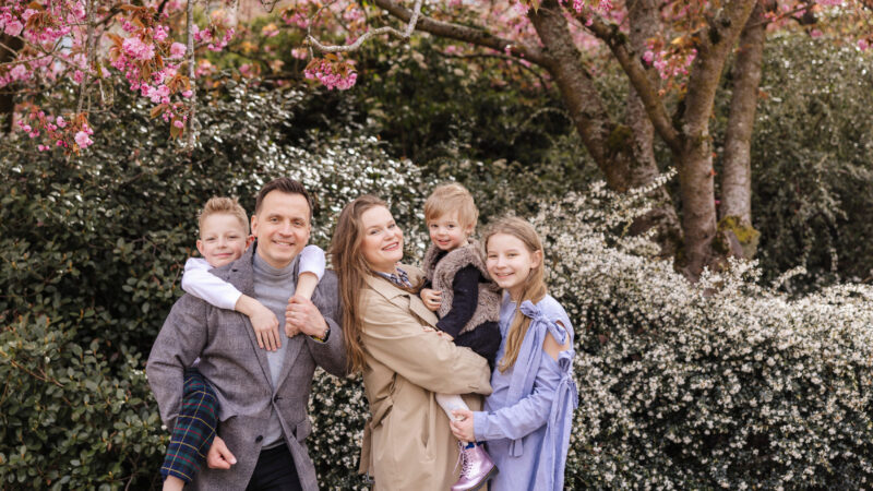 Family of five smiles in front of cherry blossoms