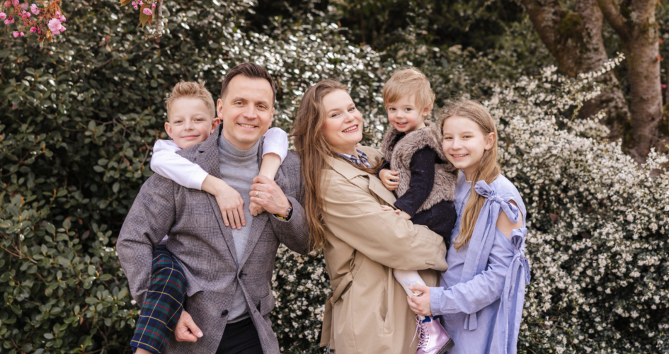 Family of five smiles in front of cherry blossoms